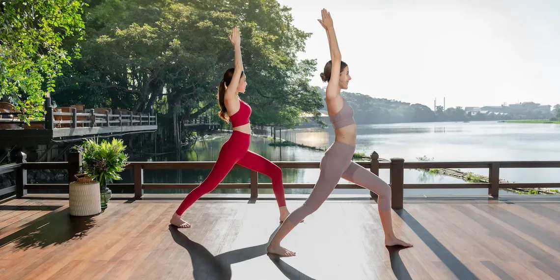 twee vrouwen doen yoga op de pier bij het water