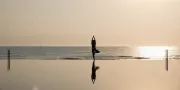 vrouw in yogapose aan het strand bij het zwembad